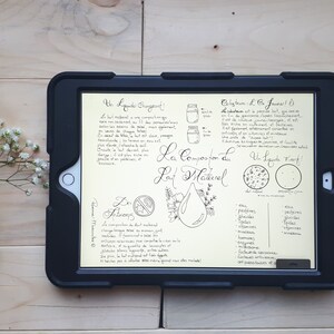 Peut inclure: Une tablette numérique avec un fond jaune et des notes manuscrites sur la composition du lait naturel. Les notes comprennent les mots français "La Composition du Lait Naturel" et "Un Liquide D'or." La tablette est sur une surface en bois clair.