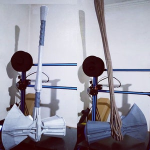 May include: A gray and white prop hammer with a twisted gray handle. The hammer head has a detailed design. The handle is approximately 36 inches long. The prop is displayed next to a brown, wooden-like prop.