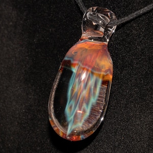 Könnte beinhalten: Ein klarer Glasanhänger mit inneren Wirbeln in Orange, Rot und Türkis. Der tropfenförmige Anhänger hängt an einer schwarzen Kordel. Das Glas hat eine glänzende Oberfläche und ist vor schwarzem Hintergrund.