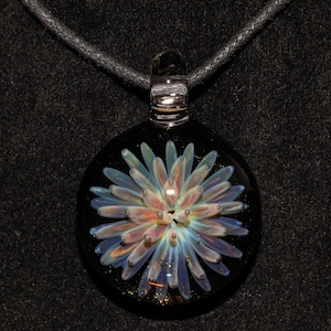May include: A round, black glass pendant with a floral design. The flower has light blue, orange, and white petals. The pendant hangs from a black cord. The glass has a clear, rounded top.