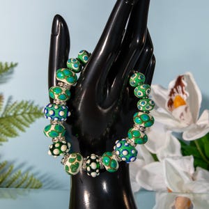 May include: A white and green beaded bracelet with silver accents. The beads are round and have a pattern of green and blue dots.