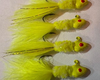 May include: Four bright yellow fishing lures with red eyes and a fluffy yellow tail. The lures are arranged in a row, with the tails facing the viewer.