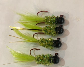 May include: Four green and black fishing lures with feathers. The lures have a black bead and a green and gold body.