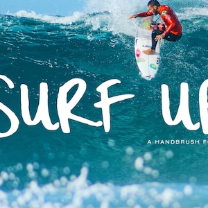 May include: A surfer in a red wetsuit rides a surfboard on a large ocean wave. The words "SURF UP" are written in large white letters across the image, with "A HANDBRUSH FONT" below.