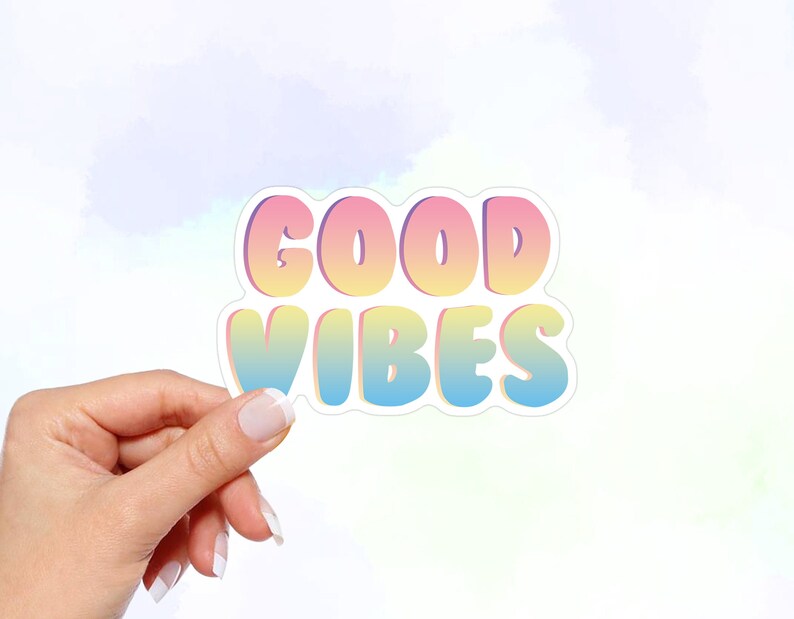 May include: A sticker with the text "GOOD VIBES" in a rainbow gradient font. The sticker has a white outline and is held in a hand.