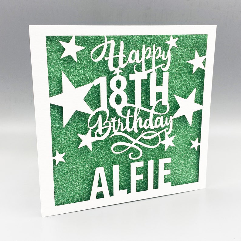May include: A white card with a green glitter background. The card has a cut-out design of stars and the text "Happy 18th Birthday Alie"