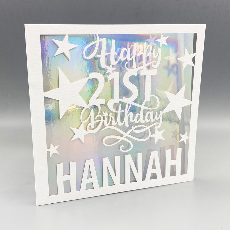 May include: White card with a cut-out design featuring stars and the text "Happy 21st Birthday Hannah". The card has a holographic background.