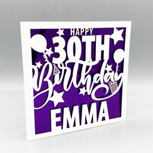 May include: A white card with a purple background and a white cutout design that says "Happy 30th Birthday Emma". The design includes stars, balloons, and a gift box.