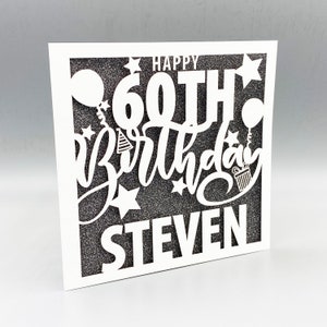 May include: A white card with a black glitter background and a white cut-out design that says "Happy 60th Birthday Steven".