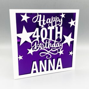 May include: A white card with a purple background and white cut-out stars. The text "Happy 40th Birthday ANNA" is cut out of the card.