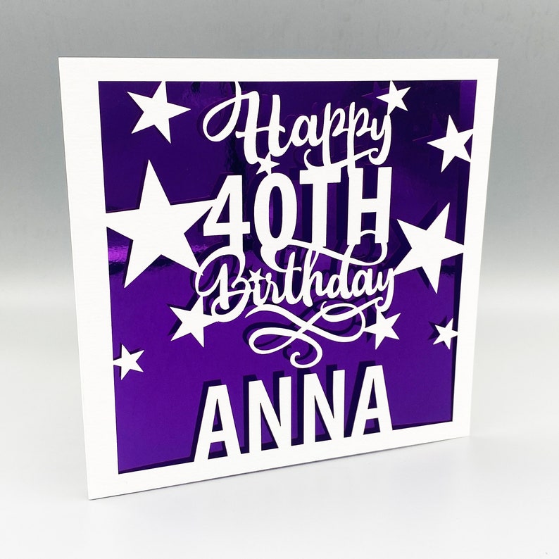 May include: A white card with a purple background and white cut-out stars. The text "Happy 40th Birthday ANNA" is cut out of the card.