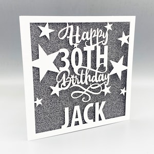May include: White card with a black glitter background and a white cut-out design that says "Happy 30th Birthday Jack" with stars around the text.
