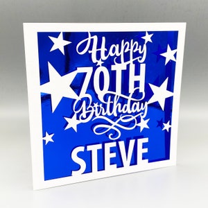 May include: White card with a blue background and white cut-out stars and the text "Happy 70th Birthday STEVE".