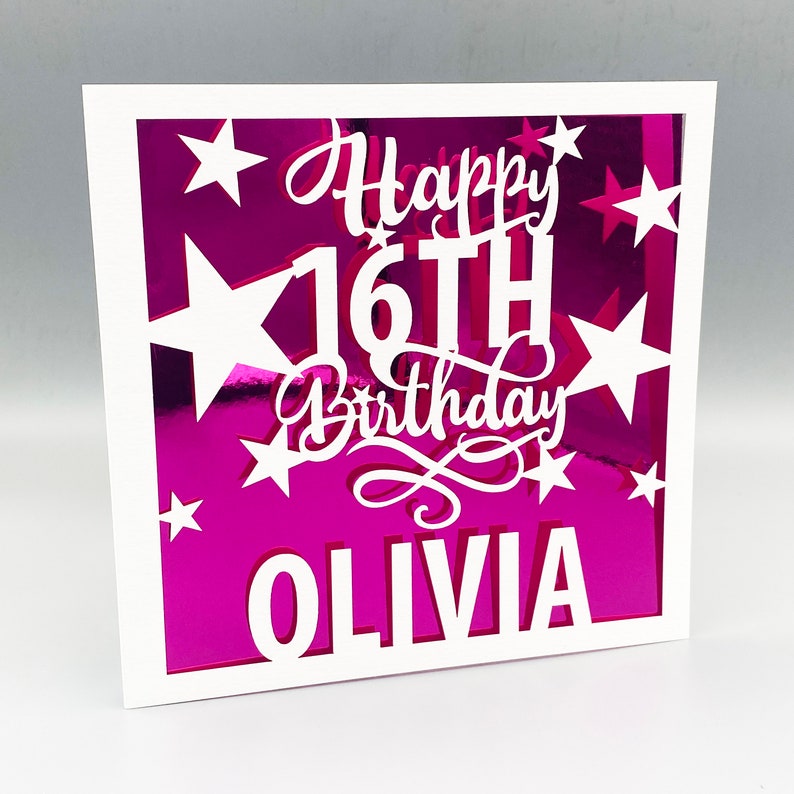 May include: A white card with a pink background and a white frame. The card has a white cutout design of stars and the text "Happy 16th Birthday Olivia".