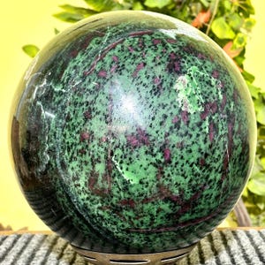 Könnte beinhalten: Eine grüne und rosafarbene Kugel mit einem gesprenkelten Muster. Die Kugel ist aus poliertem Stein und hat eine glatte, glänzende Oberfläche.