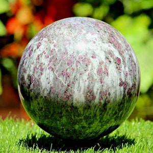May include: A large, round, polished sphere of pink and white marble with a swirling pattern. The sphere is sitting on a green surface.