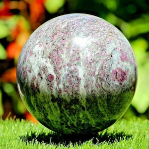 May include: A large, polished sphere of green, white, and pink marble. The sphere has a swirling pattern of colors and is smooth to the touch.