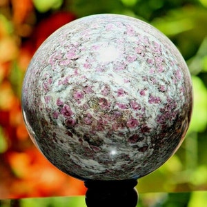 May include: A polished sphere of pink and grey marble with a swirling pattern. The sphere is on a black stand.
