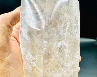 May include: A large, clear quartz crystal with a rough, natural surface. The crystal has a slightly yellow hue and is translucent. It has a pointed tip and a flat base.