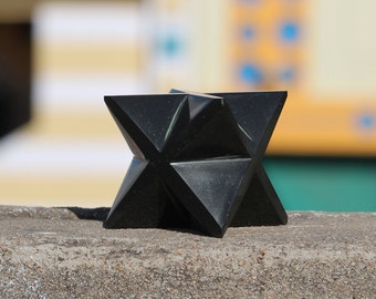 May include: A black, geometric star-shaped sculpture made of polished stone. The sculpture is sitting on a gray concrete surface.
