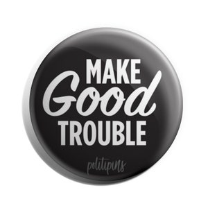 May include: Black and white button with the text "MAKE GOOD TROUBLE" in a white cursive font. The text "politipin" is in a smaller white font below the main text.