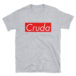 May include: A gray short-sleeved t-shirt with a red box that says "Cruda" in white text.