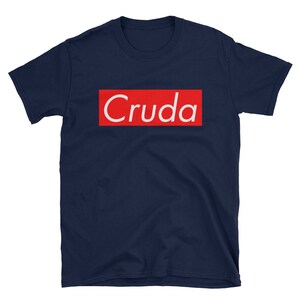 May include: A navy blue t-shirt with a red box and the word "Cruda" in white letters.