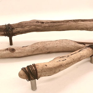 Op de afbeelding: Drie rustieke houten kastknoppen met draadaccenten. De knoppen zijn gemaakt van natuurlijk drijfhout en hebben een unieke, organische vorm. Elke knop is bevestigd aan een metalen basis.