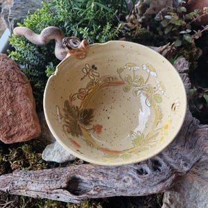 Puede incluir: Una taza de cerámica blanca con asa negra y el texto "But First, Coffee" en negrita negra. La taza se encuentra sobre un fondo borroso, sugiriendo un ambiente acogedor.