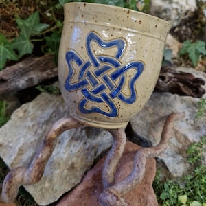 Può includere: Una tazza in ceramica con una glassa macchiettata in tonalità beige e marrone. La tazza presenta un design a nodo celtico blu.