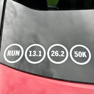May include: White vinyl decals on a car window. The decals are in white circles with the words "RUN", "13.1", "26.2", and "50K". The car is red.