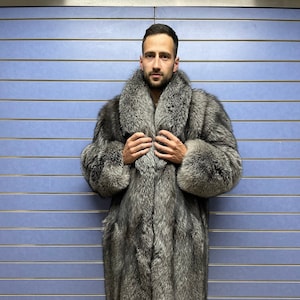 Puede incluir: Un abrigo largo de piel de color gris plateado con un cuello ancho. El abrigo se lleva con pantalones negros y zapatillas deportivas. La piel parece gruesa y lujosa, creando una pieza llamativa.