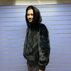 May include: A black fur bomber jacket with a hood. The jacket has a zipper closure and ribbed cuffs.