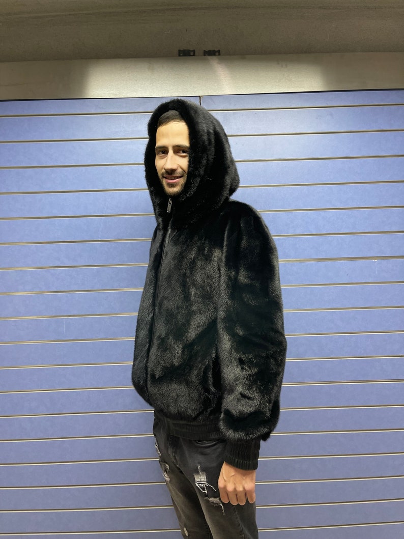 May include: A black fur bomber jacket with a hood. The jacket has a zipper closure and ribbed cuffs.