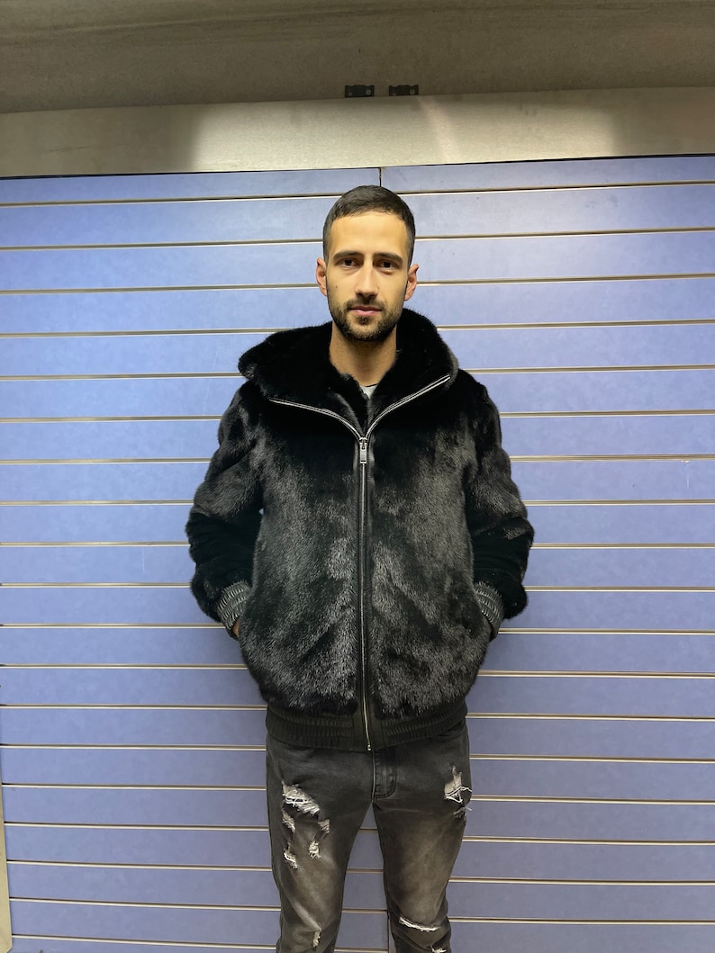 May include: A black fur bomber jacket with a zipper closure. The jacket has a stand-up collar and a ribbed knit trim at the cuffs and hem.