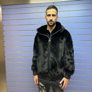 May include: A black fur bomber jacket with a zipper closure. The jacket has a hood and ribbed cuffs and waistband.