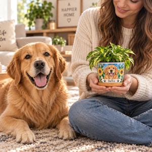May include: A ceramic plant pot featuring a colorful illustration of a golden retriever surrounded by sunflowers and green leaves. The pot displays the name Bella in black text above a small paw print icon and sits on a wooden saucer.