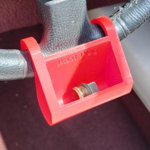 May include: A bright red plastic steering wheel lock, with the words "Beat Plug" printed on the front. The lock is attached to a black steering wheel. A metal bolt is visible inside the lock.