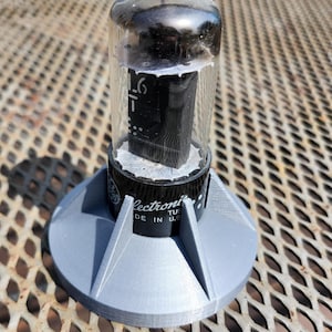 May include: A vintage vacuum tube with a clear glass enclosure and black internal components, mounted on a grey, 3D-printed base. The tube has the text "-1 6" printed on it, and the base has the text "Electronic Tube Made in U.S."