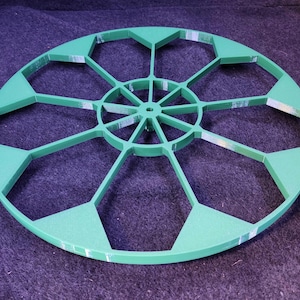 May include: A green plastic circular template with 12 octagonal cutouts. The template has a central hub with spokes radiating outward.