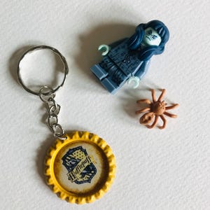 May include: A yellow bottle cap keychain with the Hufflepuff crest, a blue Lego minifigure of a witch, and a brown spider.