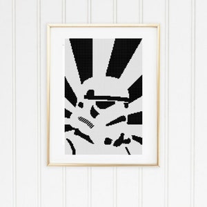 以下が含まれることがあります： 金色のフレームに入った抽象的なアートプリント。アートワークは、サンバーストパターンとさまざまな形状を備えた白黒の幾何学模様を特徴としています。プリントは、垂直パネルのある白い壁に表示されます。