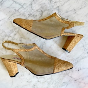 Puede incluir: Un par de sandalias de tacón de corcho y malla con una correa de slingback. Las sandalias son beige y tienen un tacón de corcho.