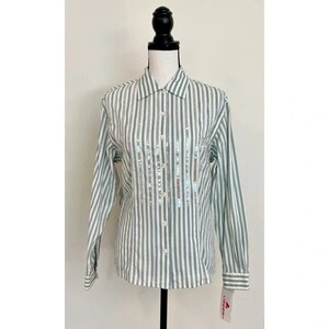 Può includere: Una camicia a maniche lunghe con bottoni, a righe bianche e grigie, con un design di paillettes sul davanti. La camicia ha un colletto e una chiusura con bottoni. L'etichetta del marchio è visibile nell'angolo in basso a destra della camicia.