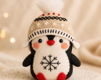 May include: A felt penguin ornament featuring a black and white body, red feet, and a red beak. The penguin wears a tan knit-style hat with a white pom-pom, black and white stitched patterns, and a black snowflake embroidery on its white belly.