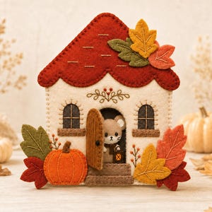Peut inclure: Une maison en feutrine avec un toit rouge, des murs crème et deux fenêtres arquées. Une petite souris se tient dans l'embrasure de la porte ouverte, tenant une lanterne. La maison est décorée de citrouilles orange et de feuilles d'automne.