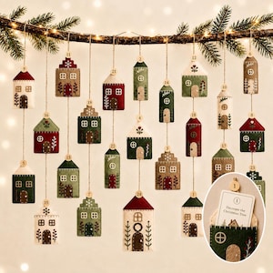 Puede incluir: Un calendario de adviento colgante con veinticuatro casas de fieltro en tonos rojo, verde y crema. Cada casa cuelga de una rama mediante un cordel y tiene una etiqueta de madera numerada. Una pequeña tarjeta muestra Decorate the Christmas Tree.