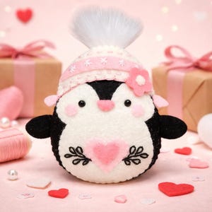 Valentine's Penguin felt ornament with pink hat, heart detail, and embroidery. DIY felt sewing pattern and SVG for Valentine's Day decor, love gifts, or easy craft projects. Perfect for beginners and experienced crafters to create a handmade decor