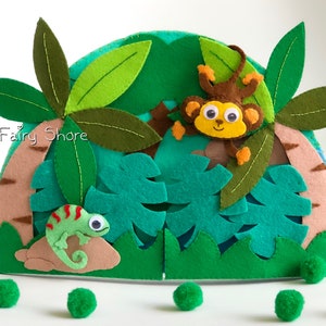Peut inclure: Une scène de jungle en feutre avec un caméléon vert, un singe aux grands yeux et des palmiers. La scène est en feutre et a un tronc brun et des feuilles vertes. Le singe est brun avec des accents jaunes et le caméléon est vert avec des rayures rouges. La scène est parfaite pour la chambre d'un enfant ou sa salle de jeux.