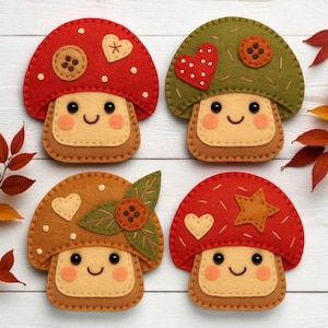 Op de afbeelding: Vier vilten paddenstoeldecoraties in rood, groen en bruin. Elke paddenstoel heeft een lachend gezicht, een knoop en hart- of steraccenten. De paddenstoelen liggen op een wit houten oppervlak met herfstbladeren.